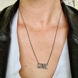 A silver necklace with the word 'LOVE' crafted in textured metal with vine details, connected to a border with small balls, on a diamond-cut cable chain on a person's neck
