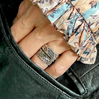 A set of 3 Karen Karch silver bands with repeating ball details on one side, both sides, and on the top stacked on a hand with a Bsilver lack Diamond-Studded Signet Wrap Ring.