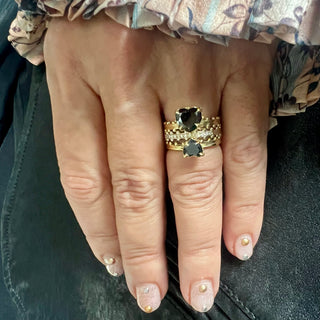A three-ring stack with the top and bottom rings featuring heart-shaped black diamonds in gold settings, and the center ring with diamond-studded half-eternity in 18kw on a hand.