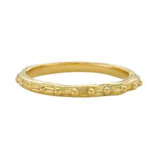 A Karen Karch 18k yellow gold band  with a textured surface and ball embellishments along the circumference on a white background.
