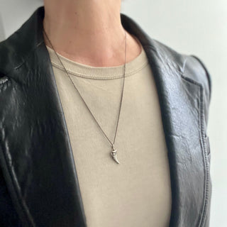 Silver horn-shaped pendant with angular raised shapes on a white background