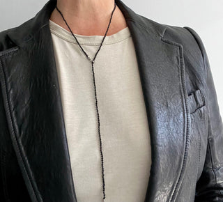 A close-up of a person wearing a black leather jacket and a black spinel beaded necklace with a weathered texture silver closure.