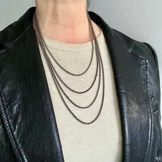 A close-up image of a person wearing avarious lengths of a Karen Karch silver 2.8mm cable chain necklace with a lobster lock clasp.