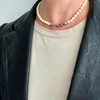 A pearl choker necklace on the neck with a black diamond silver clasp and handmade cube silver beads.