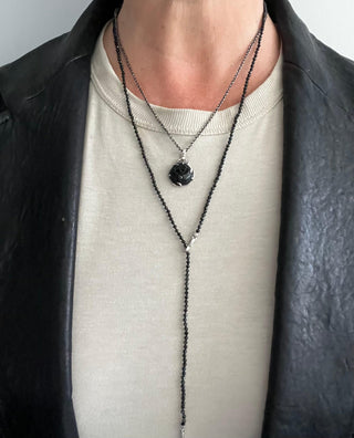 A black spinel silver lariat necklace with a weathered texture closure, featuring a loop and a pull-through bar styled with a black onyx rosebud amulet