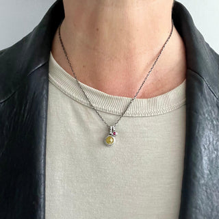 Karen Karch Double Inner Circle Silver Necklace with One Large Yellow Diamond Charm and One Small Ruby Charm on person in leather jacket