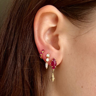 Karen Karch dangling diamond earrings with a line of three distinct shapes, each with a central diamond, set in gold claw settings on ear styled with Ruby Marquise gold drop earrings and ruby studded vine sleeper hoop
