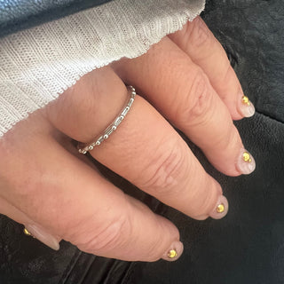 A Karen Karch platinum band with a textured surface and ball embellishments along the circumference on a hand.