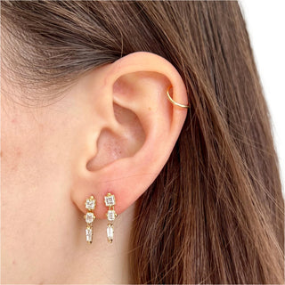 A pair of Karen Karch dangling diamond earrings with a line of three distinct shapes, each with a central diamond, set in gold claw settings paired together on ear