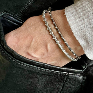 A pair of Karen Karch silver oval bangles with repeating ball details, displaying a weathered texture and irregular edges on wrist.
