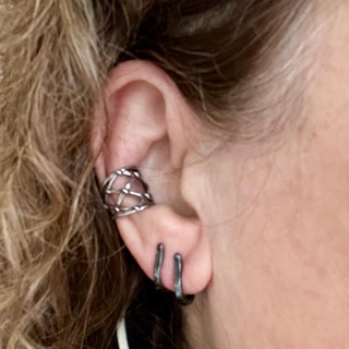 A pair of blackened silver cuff hoop earrings with a textured surface on the ear styled with fishnet vine cuff hoops