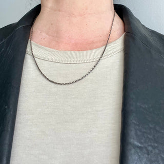 A person wearing a 20" oxidized silver diamoind cut cable chain necklace