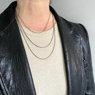 A person wearing  3 different lengths of an oxidized silver diamond cut cable chain necklace