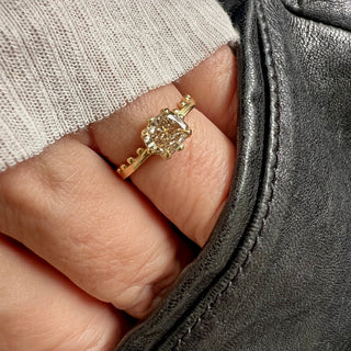 An 18k yellow gold ring by Karen Karch with a cushion-cut champagne diamond set in a four-claw demi-bezel setting, featuring a weathered texture band with ball details on a hand.