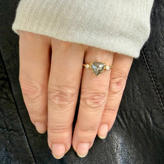 Karen Karch 18k Dark Grey Trilliion Diamond held by 4 claws with a colorless diamond on each side on a weathered gold band shown on a hand. 