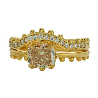 A curved, yellow gold band by Karen Karch with a row of ball details on one side, studded with colorless diamonds half way stacked on a cushion cut champagne diamond solitaire on white background. 