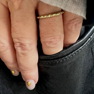 A Karen Karch 18k yellow gold band  with a textured surface and ball embellishments along the circumference on a hand.