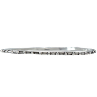 A Karen Karch oval shape silver bangle bracelet with a repeated ball detail along the edge, displayed on a white backround.