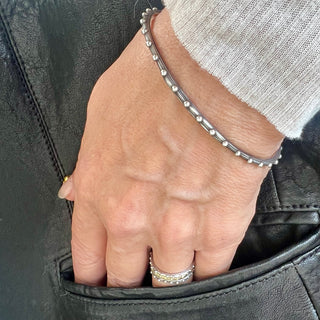 A Karen Karch oval shape silver bangle bracelet with a repeated ball detail along the edge, displayed on a wrist.