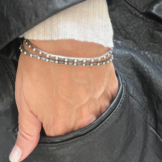 A Karen Karch silver bangle bracelet with a repeated ball detail along the edge, displayed on a wrist.