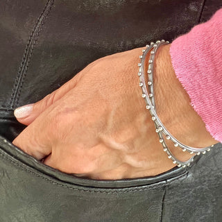 A set bof Karen Karch silver bangles bracelet with a repeated ball detail along the edge, displayed on a wrist