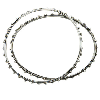 Two silver bangles by Karen Karch, one with a round shape and the other with an oval shape, both featuring a weathered texture and embellished with repeating ball details, overhead view.