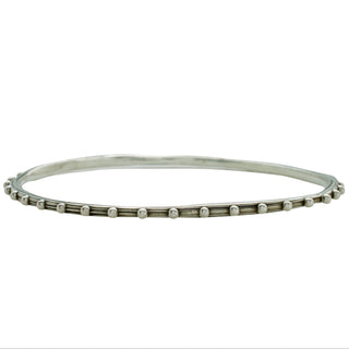 A Karen Karch round shape silver bangle bracelet with a repeated ball detail along the edge, displayed on a white backround.