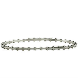 A Karen Karch oval-shaped silver bangle bracelet with a weathered texture and repeating ball details on each side on white background.