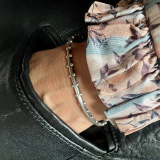 A Karen Karch oval-shaped silver bangle bracelet with a weathered texture and repeating ball details on each side on wrist