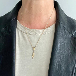 A gold-filled chain necklace with a 10ky skull design at the center and a wing charm by Deme Wolfe for Karen Karch on a person