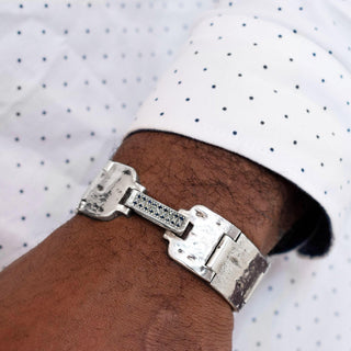 A 20mm wide weathered silver Mainstay bracelet with a studded clasp featuring black and white diamonds, designed by Karen Karch on a person in a white polka dot shirt.