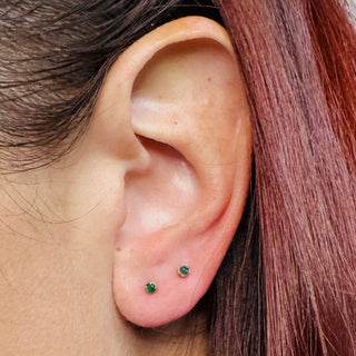 Pair of Karen Karch green emerald gemstone studs in a rose gold claw setting on an ear.