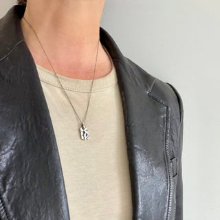 Karen Karch Unearthed Heavily Textured Dog Tag in sterling silver on a chain on a person.