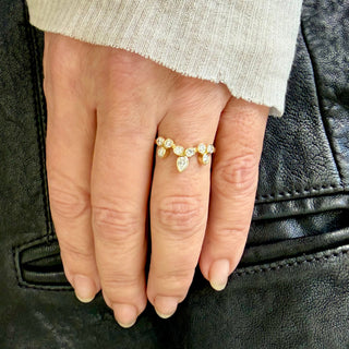A Karen Karch 18k yellow gold ring with round diamonds configured in the shape of a tiara featuring a central pear shape diamond with 8 smaller round diamonds set in bezels on a hand. 