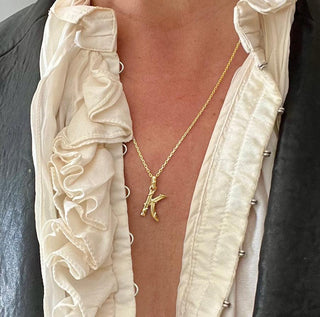 Karen Karch textured 10k yellow gold charm in the shape of the letter 'K' with a vine-detail and rectangular bail on a person.