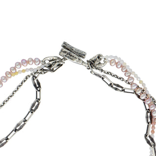 Four distinct strands—pink freshwater pearls, delicate shaded pink opal beads, with two unique silver chains - create a chic tangled necklace united with a substantial weathered toggle closure shown close up on a white background. 