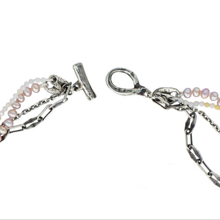 Four distinct strands—pink freshwater pearls, delicate shaded pink opal beads, with two unique silver chains - create a chic tangled necklace united with a substantial weathered toggle closure shown open close up on a white background. 