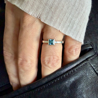 Karen Karch Silver ring with an Aquamarine Princess Cut Square gemstone on an irregular polished band side view on a hand.