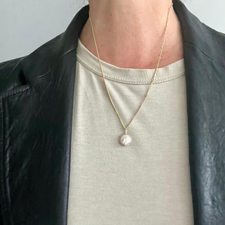 Karen Karch by Deme Wolfe  double-sided freshwater pearl charm with claws on both sides, set in a 10k gold colored metal frame with black diamonds studded on the front claws on chain on a person