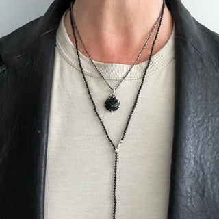 Karen Karch silver charm with a green jade rosebud carving on a vine detailed bail layered with Black spinel bead lariat necklace on a person.