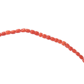 A close up of small barrel shape coral-red beads , knotted between with matching thread, arranged in a gentle curve against a solid white background.