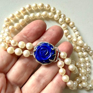Karen Karch custom carved lapis rose centerpiece clasp on double strand of pearls with a hand holding it.