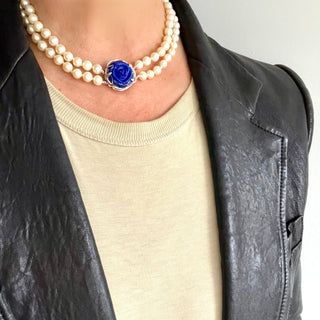 Person wearing a pearl necklace with a blue lapis rose clasp and a black leather jacket and beige t-shirt.