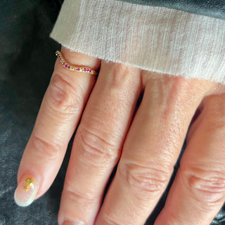 A Karen Karch by Deme Wolfe 14k yellow gold ring with rubies on the front of a curved band on a pinky finger.