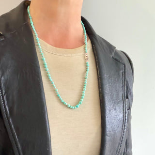 Karen Karch 4mm and 5mm Round Mixed Size Turquoise Beaded Necklace with a small silver tag engraved with a K-rose logo on a neck.