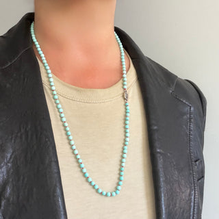Karen Karch 4mm Round Turquoise Beaded Necklace with a hot pink knot between each bead with a small silver tag engraved with a K-rose logo on a neck.