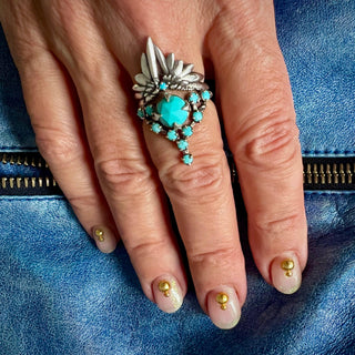 A Karen Karch silver cocktail ring featuring a large round turquoise center stone surrounded by smaller turquoise stones, in a star-like formation stacked with a Silver Turquoise Winged Ring on a hand.