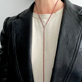 A person wearing a black leather jacket and a silver garnet beaded lariat necklace 
