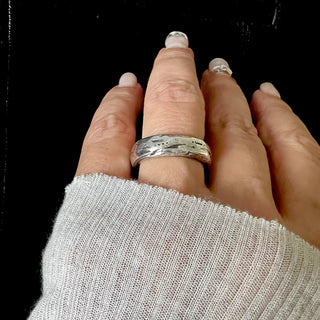 A Karen Karch silver domed weathered band with an irregular rounded edge on a hand. 