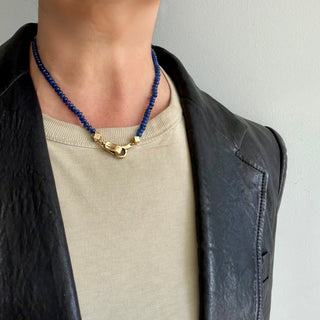 A Karen Karch Blue Sapphire beaded necklace with a 10k yellow gold weathered clasp centered in front on a person in a tshirt and leather jacket.